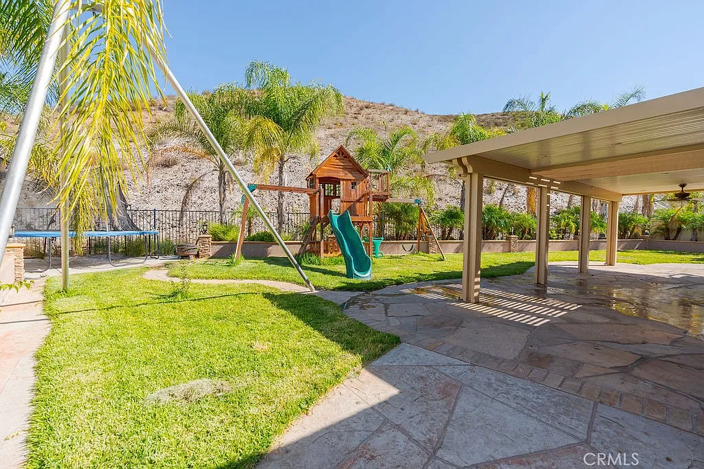 Backyard with grass, playground slide, palm trees, and hillside.
