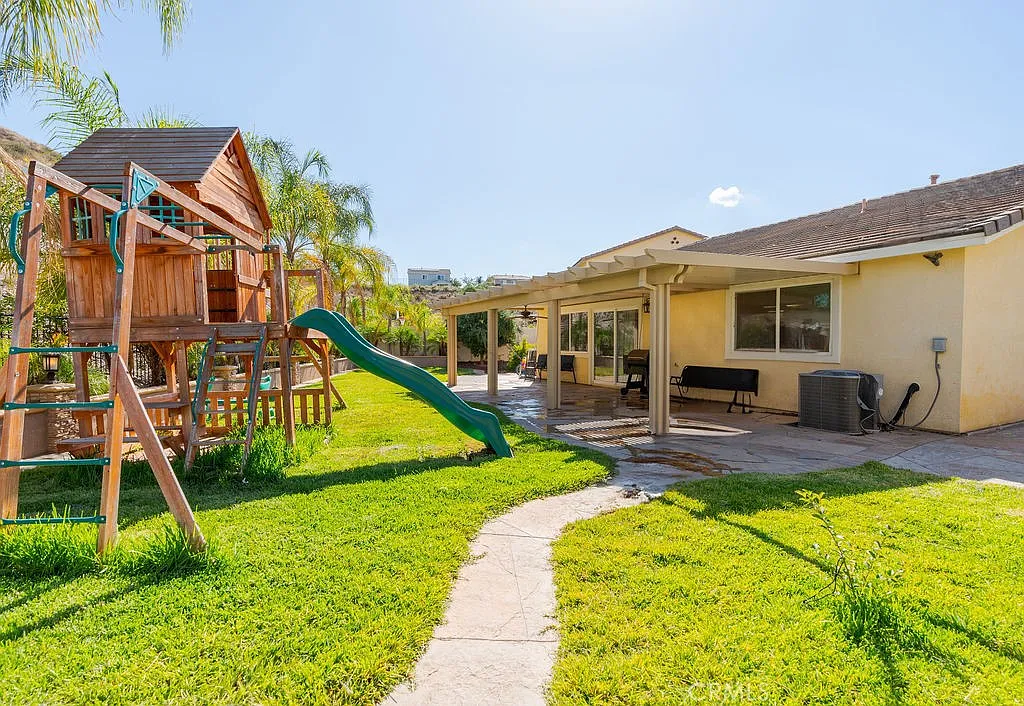 Backyard with grass, playground slide, swings, patio, and house.