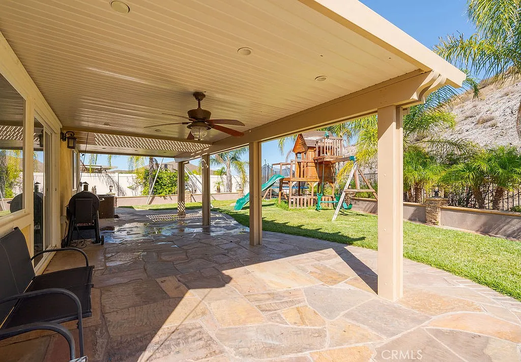 Patio with chairs overlooking backyard playground with slides, swings, and plants.