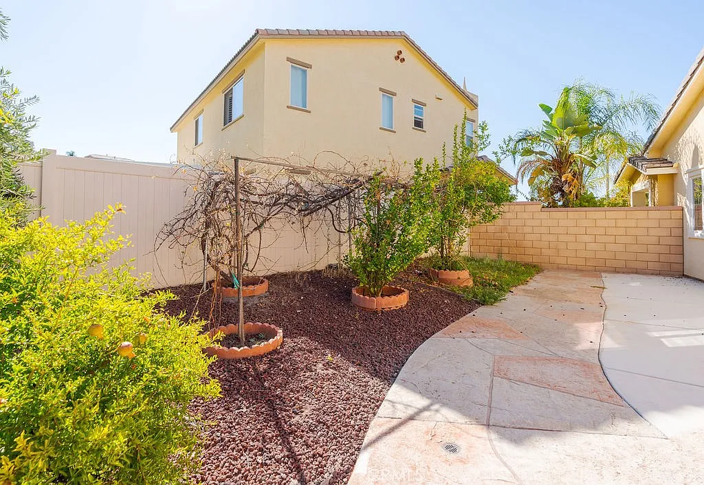 A backyard with a two-story house, small concrete patio, and landscaped areas with plants and trees.