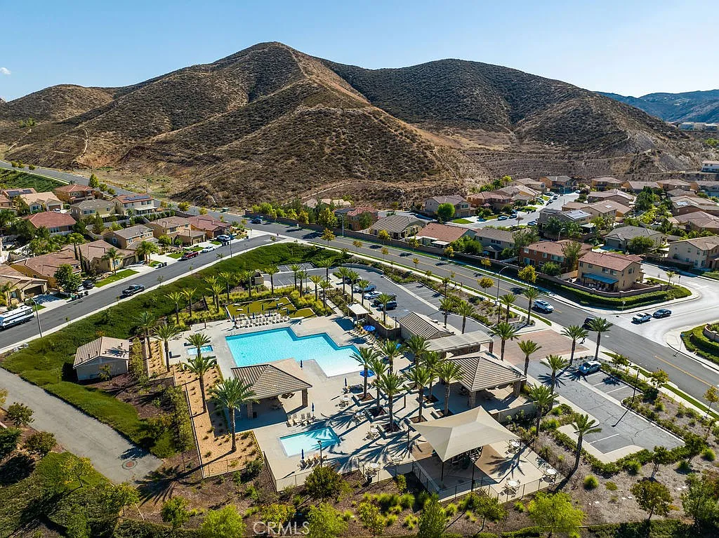 Aerial view of a residential neighborhood with a community pool, palm trees, and surrounding hills.