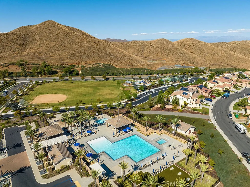 Aerial view of a residential area with a large swimming pool, palm trees, and mountains in the background.