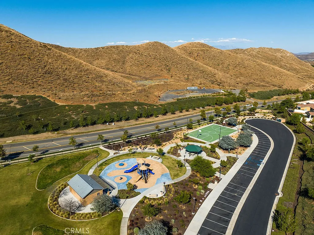 Aerial view of park with playground, sports courts, road, and hills.