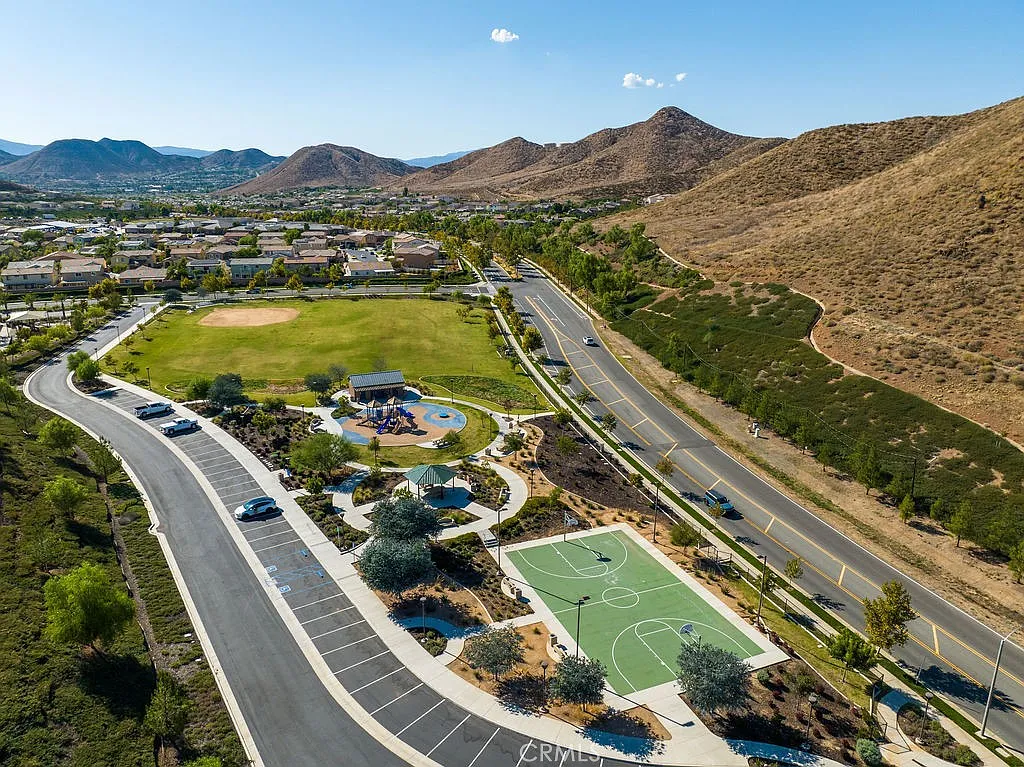 Aerial view of park with playgrounds, sports courts, hills, and nearby homes, real estate.