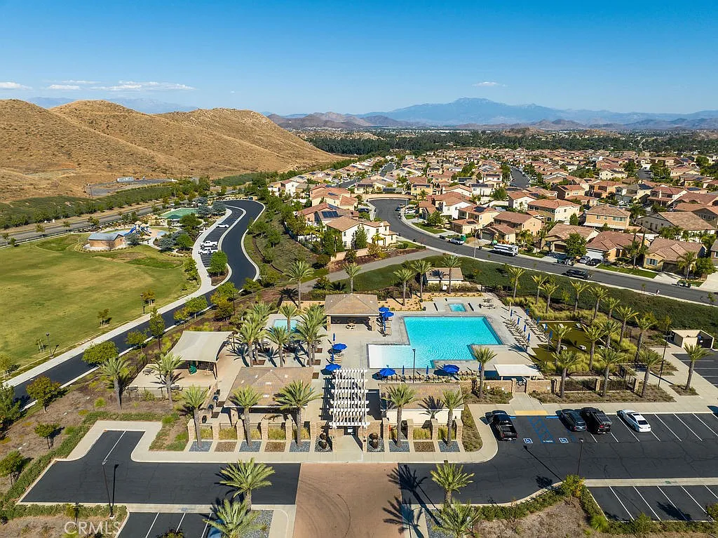 Aerial view of a neighborhood with swimming pools, palm trees, and surrounding hills.