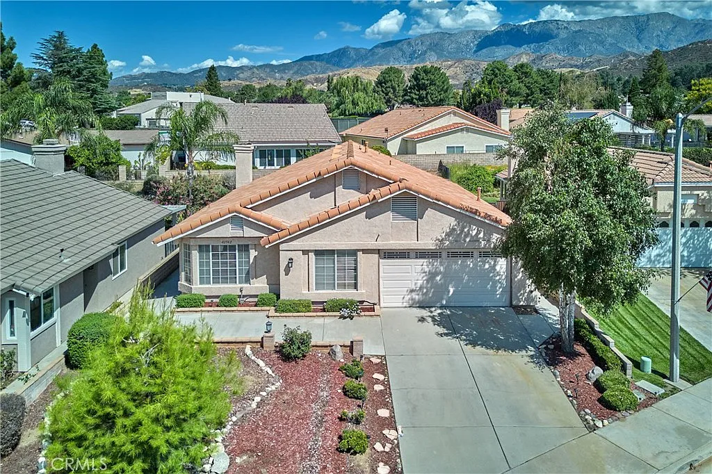 Aerial view of house with landscaped front yard, shrubs, trees, mountains, and blue sky, California real estate.