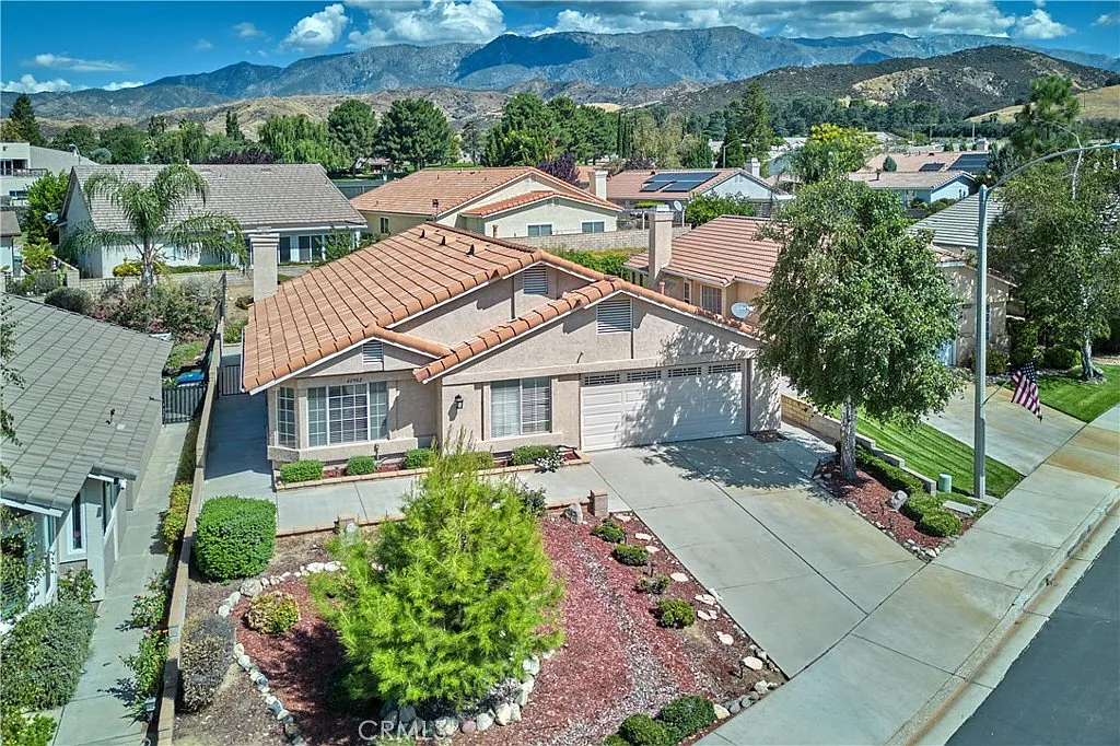 Aerial view of single-story house with tan roof, landscaping, and mountains in the background, California real estate.
