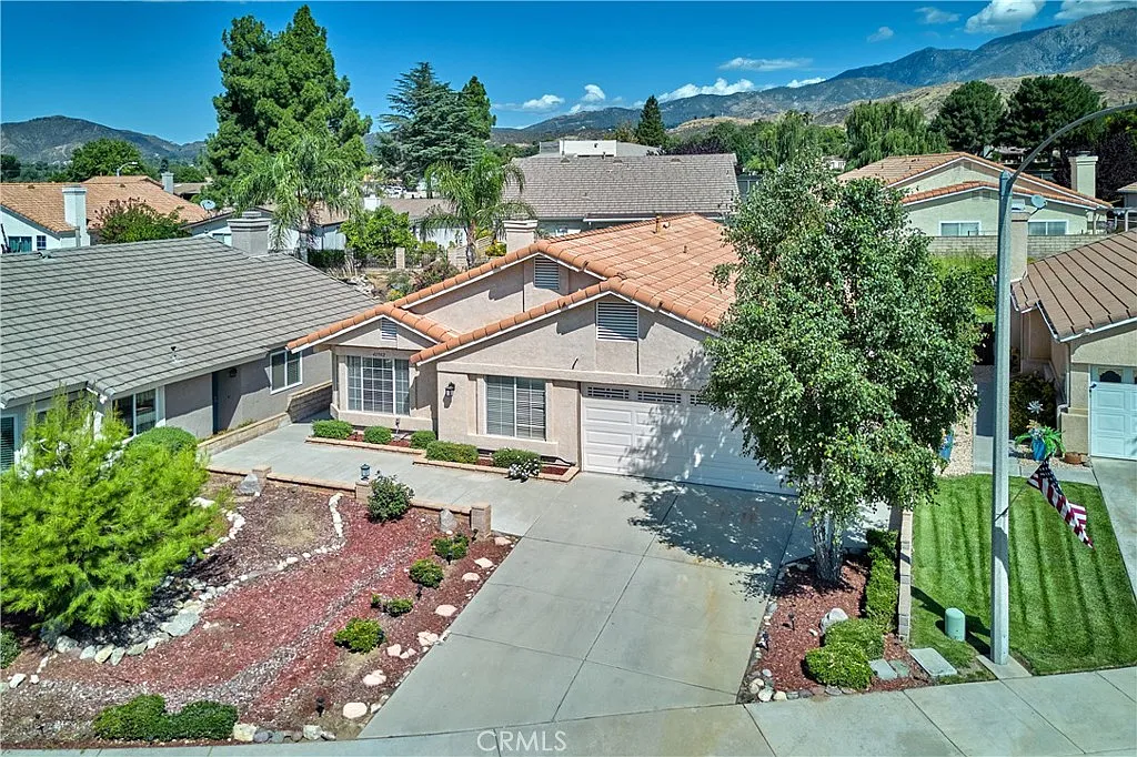Aerial view of single-story house with red tile roof, landscaped gardens, and driveway, California real estate.