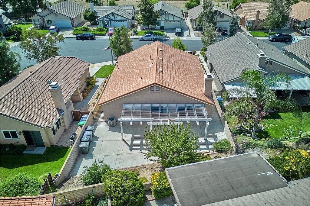 Aerial view of suburban homes with red tile roof, patio, and surrounding greenery, California real estate.