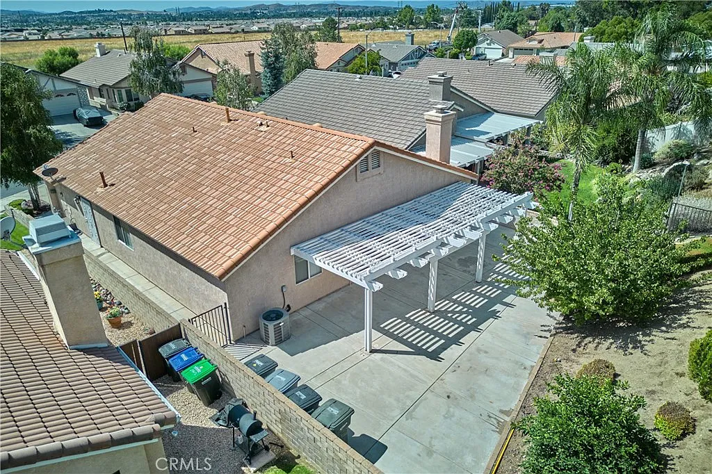 Aerial view of neighborhood with houses, red tile roofs, pergola patio, and green plants and trees, California real estate.