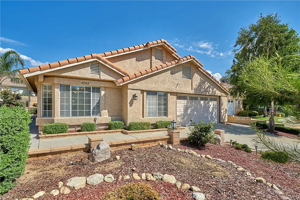 Single-story home with tiled roof, large front windows, shrubs, decorative rocks, and well-kept yard, California real estate.