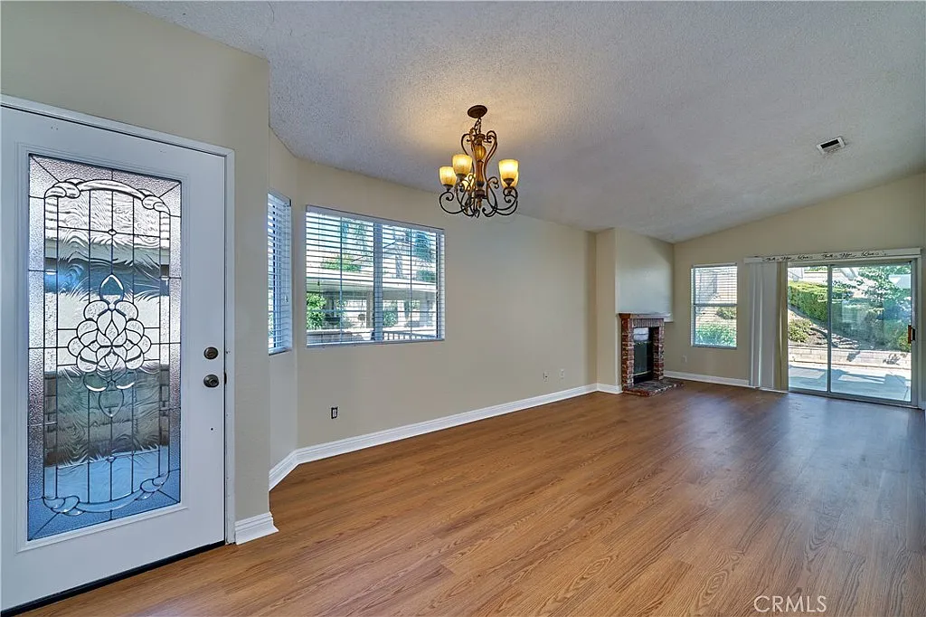 Living room with hardwood floor, large window with blinds, chandelier, fireplace, and sliding glass door to outdoor area.