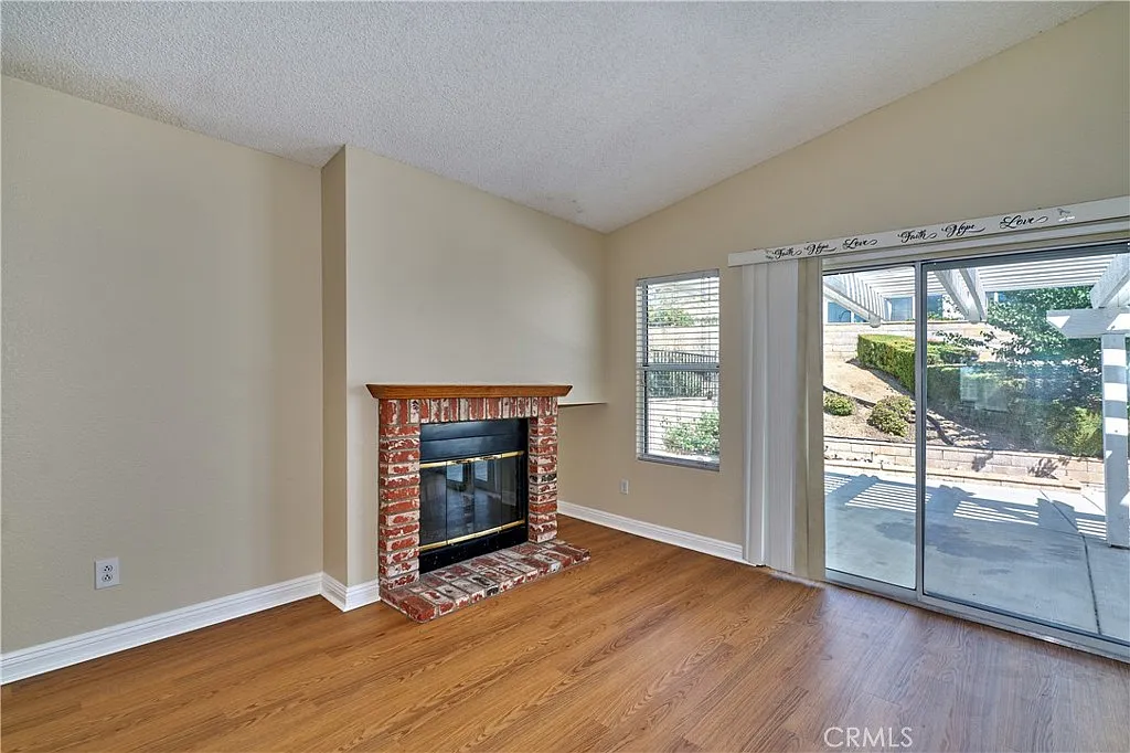 Room with wooded floor, brick fireplace, and large sliding glass doors to outdoor area.