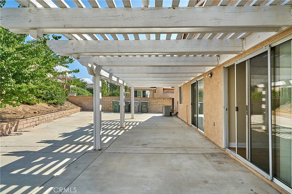 Patio with pergola, concrete floor, sliding glass doors, and green trash bins