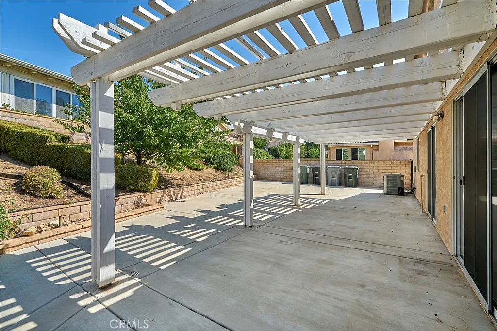 Patio with concrete floor, shadows, and surrounding greenery and walls, California real estate.