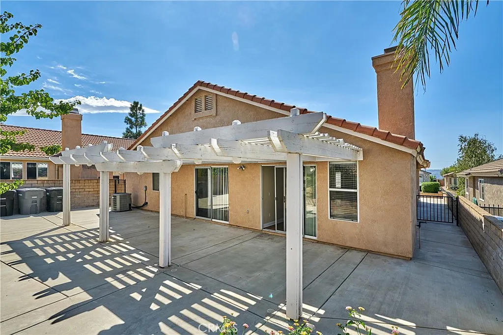 Backyard with concrete patio, white pergola, and single-story house with tiled roof and large windows, California real estate.