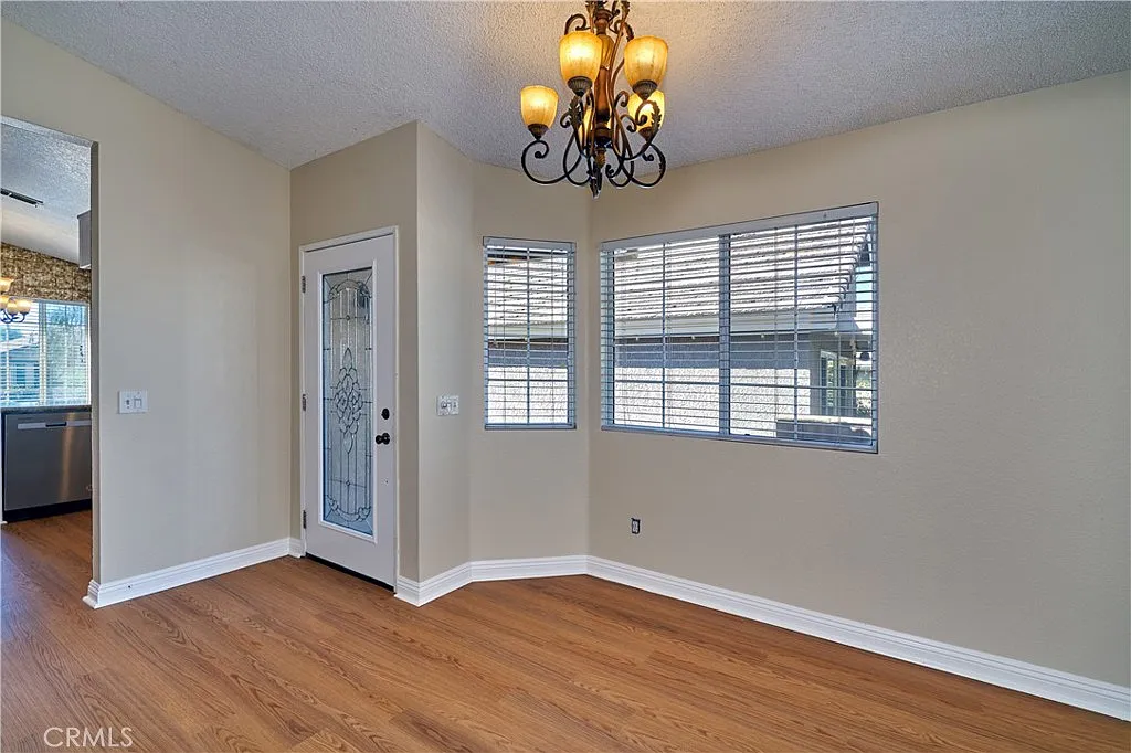 Room with chandelier, door, multiple windows, wooden floor, and neutral-colored walls