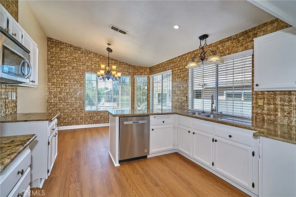 Kitchen with white cabinets, stainless steel dishwasher, gold patterned walls, chandelier, and large windows
