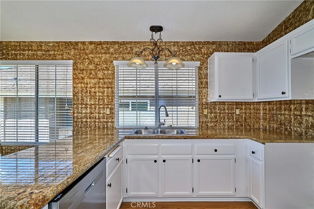 Kitchen with white cabinets, granite countertop, and large windows with blinds.