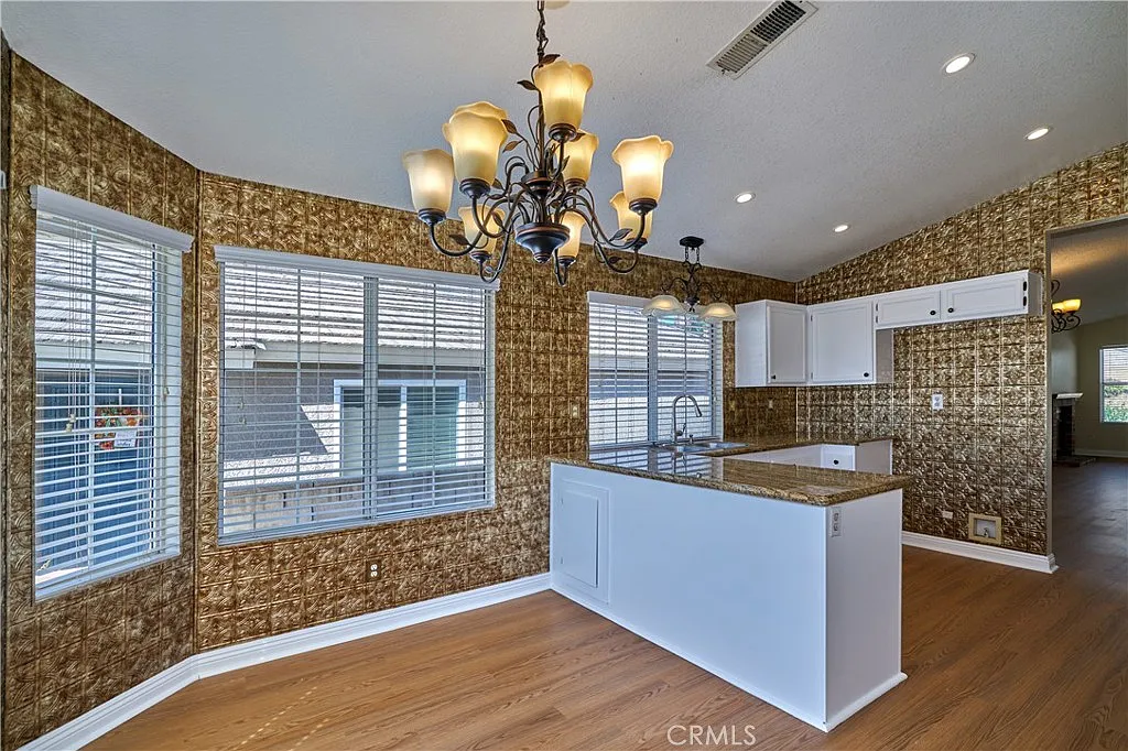 Kitchen with chandelier, white cabinets, golden patterned walls, large windows, and wooden floor.
