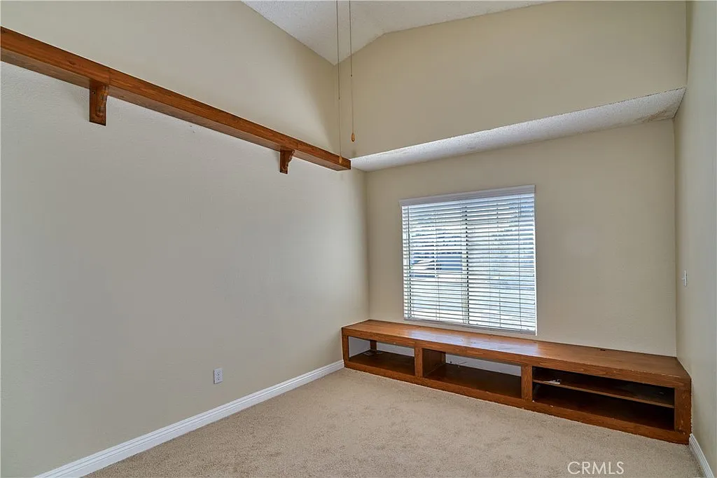 Room with beige walls, tall ceiling, window with blinds, wooden shelf, and built-in bench.