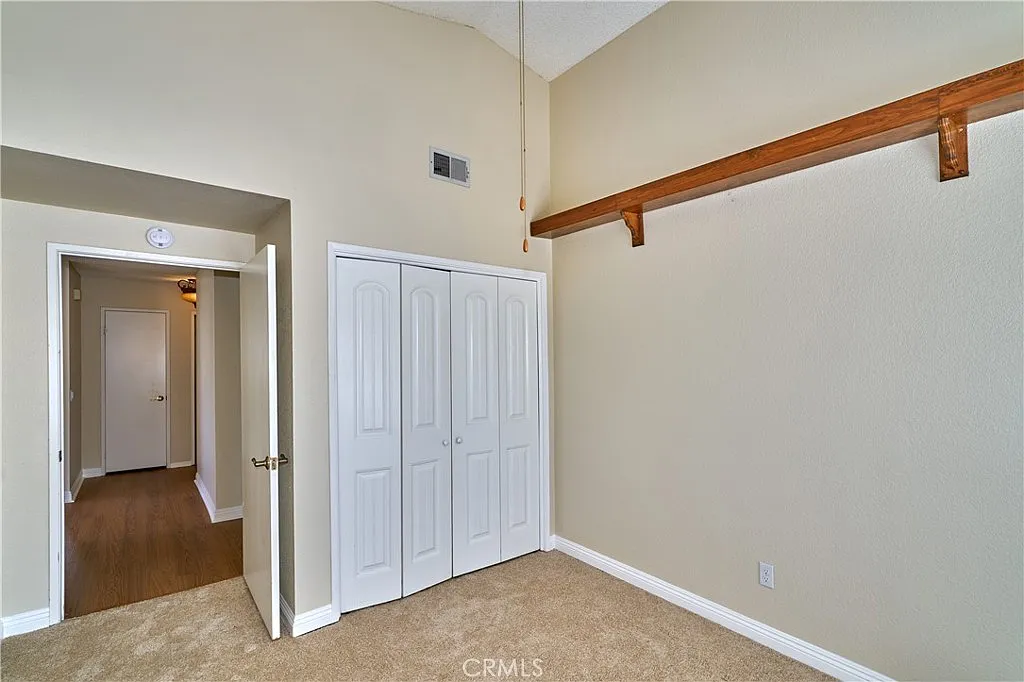 Room with high ceiling, two white closets, doorway to another room, wooden shelf, and beige carpet.