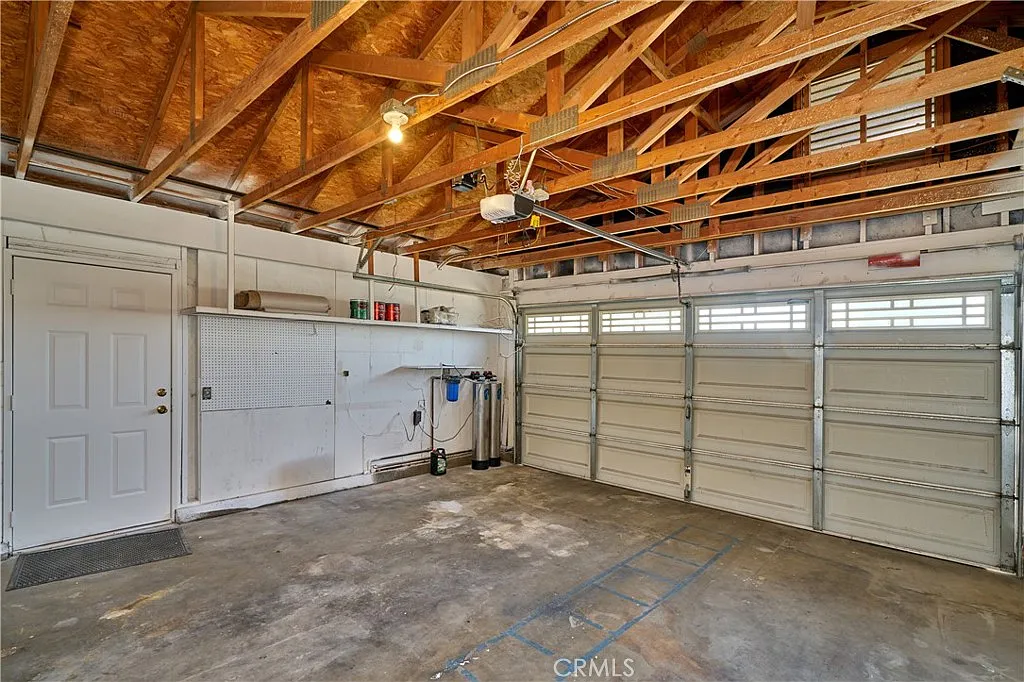 Spacious garage with concrete floor, two garage doors, shelves, overhead beams, and natural light.