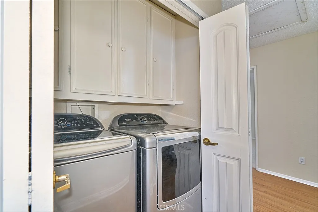 Laundry room with stacked washer and dryer, beige walls, cabinets above, and a partially open door.