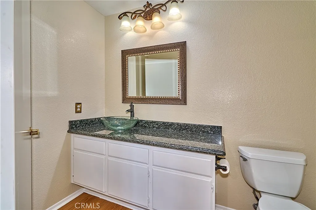 Bathroom with granite countertop, glass sink, mirror, toilet, and beige walls.