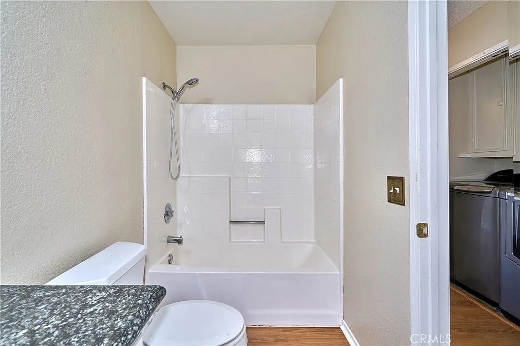 Bathroom with shower and bathtub, light walls, granite countertop, and washer and dryer.