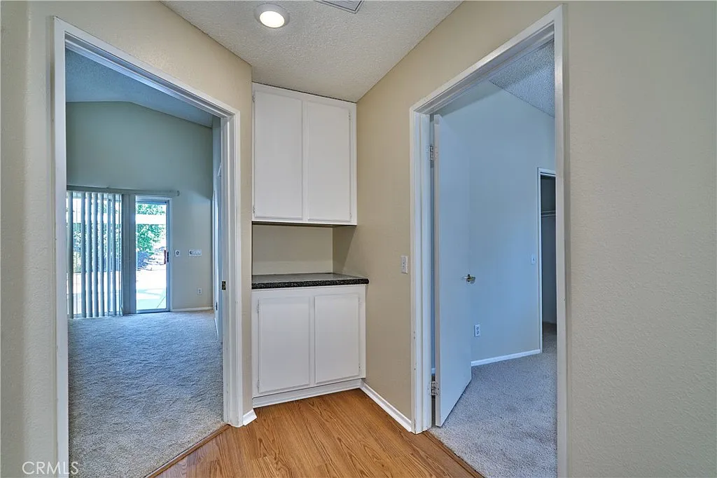 Hallway with two doorways, light walls, wooden floor, and a cabinet on the left.