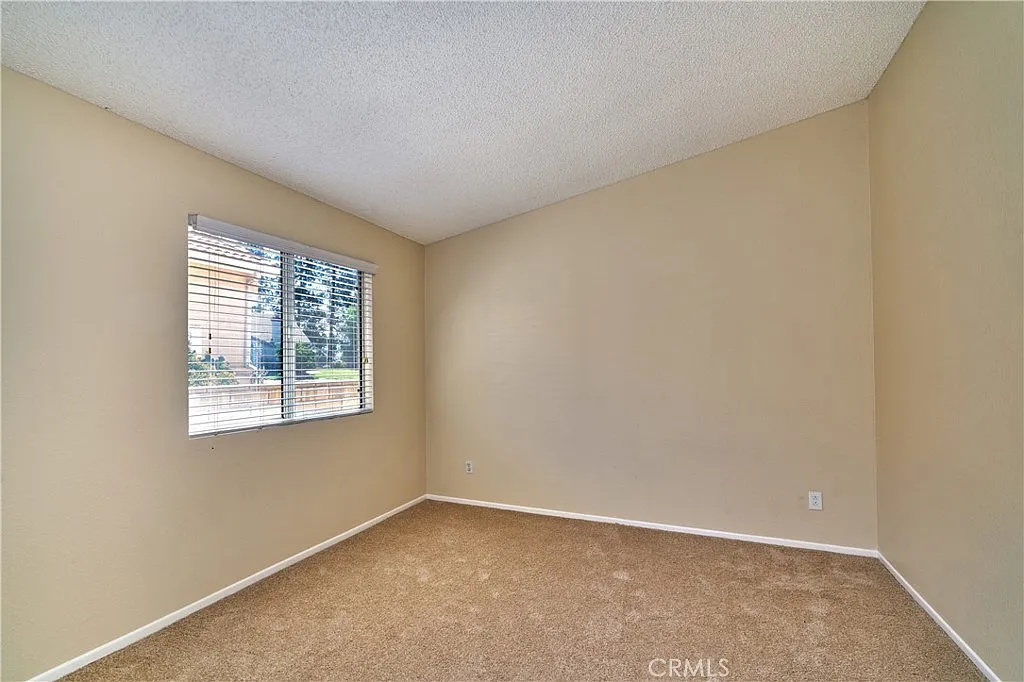 Empty room with beige walls, window with blinds, and carpeted floor.