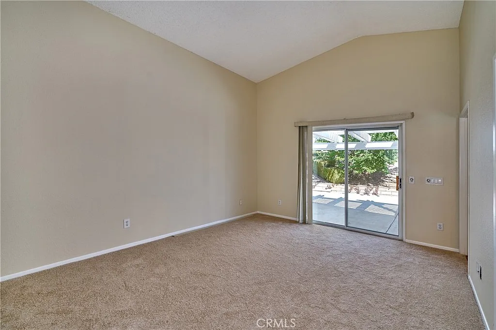 Empty living room with beige walls, carpet, and sliding glass door to outdoor area.