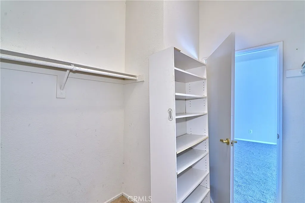 Closet interior with white shelves and a door to another room.