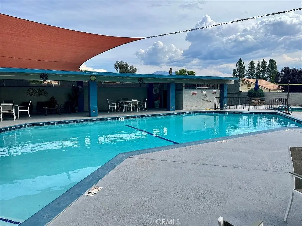 Swimming pool area with lounge chairs, shade structures, fence, and trees.