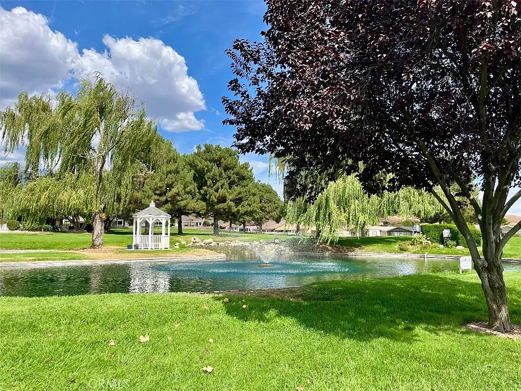 Park with a pond and fountain, green lawns, trees, and a distant gazebo