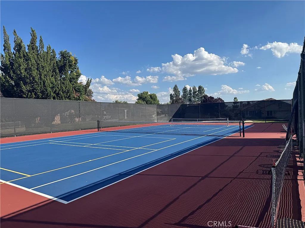 Tennis court with blue and red surfaces, surrounded by trees and a fence.