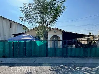House with green fence, blue tent in the yard, under clear sky, California real estate.