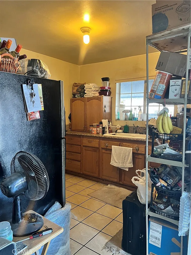 Cluttered kitchen with wooden cabinets, countertop with items, shelves with boxes, window, and scattered floor objects.