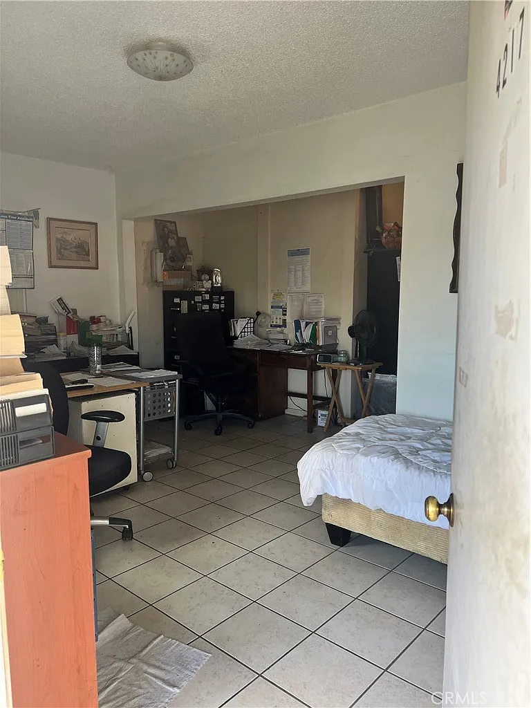 Small room with bed, desk, office furniture, and scattered papers and supplies