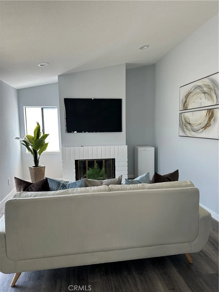 living room with white couch, wall-mounted TV, fireplace, decorative pillows, potted plant, gray walls, and wooden floor