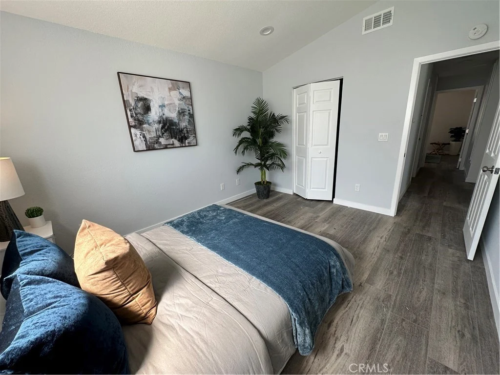 Bedroom with bed, blue and gray bedding, decorative pillow, plant in corner, light walls, and door to another room