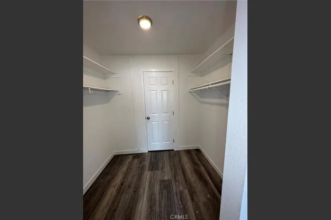 Small empty closet with white walls, wood-like floor, shelves on both sides, and closed door at back