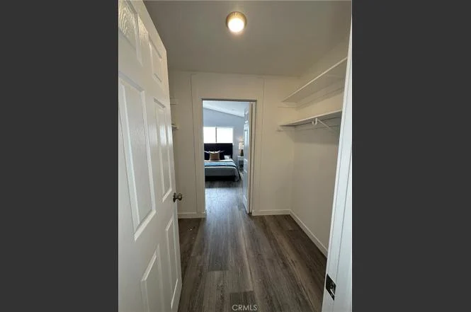 Hallway with closet on left, light-colored walls and floor, leading to bedroom
