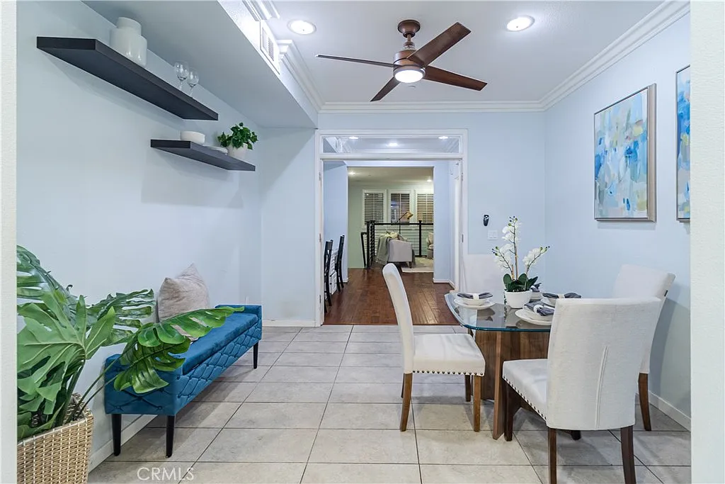 Dining area with round table, white chairs, blue bench, plants, light blue walls, tile floor, and ceiling fan.