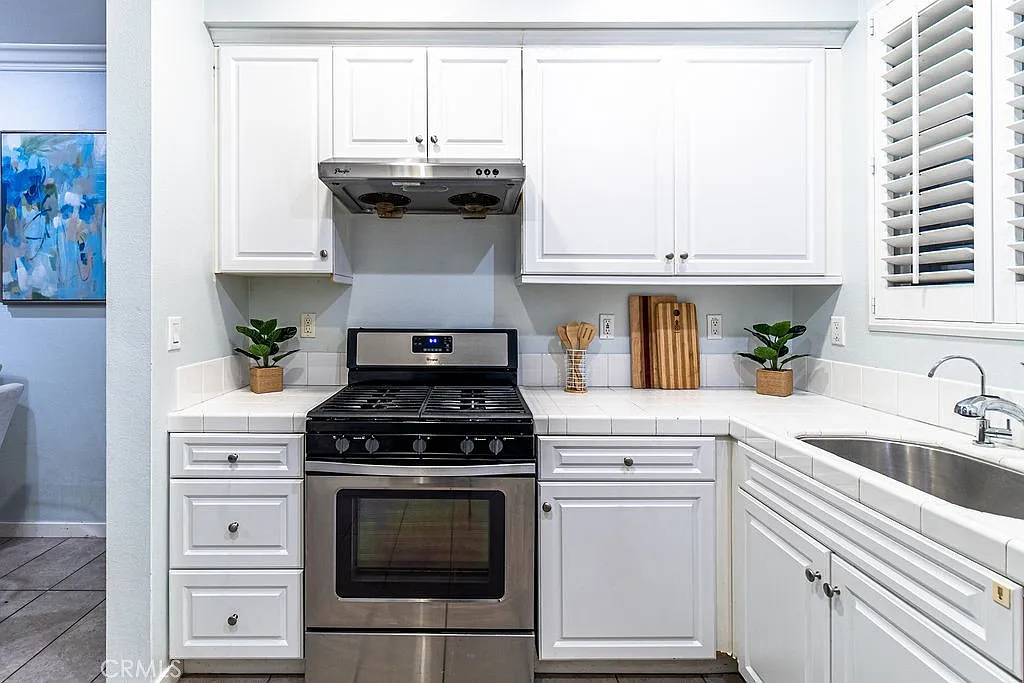 kitchen with white cabinets, stainless steel stove and sink, plants, and wooden cutting boards.