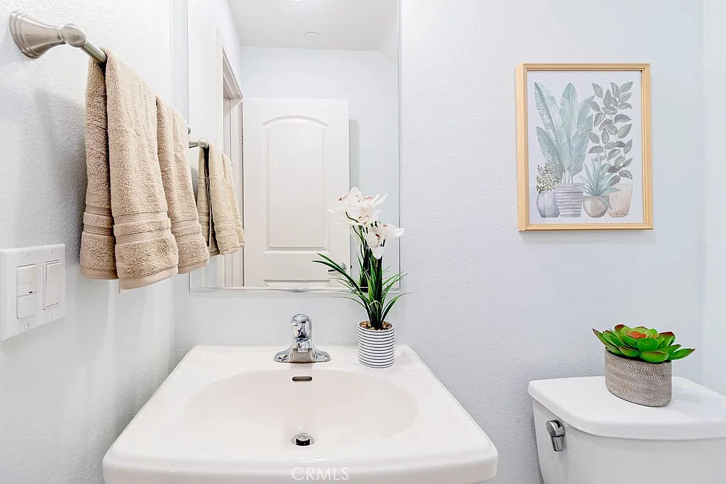 bathroom with white sink, beige towels, potted plant, and framed plant artwork