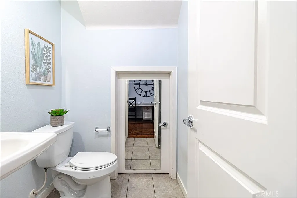 bathroom with light blue walls, white toilet and sink, wall art, mirror, and tiled floor.