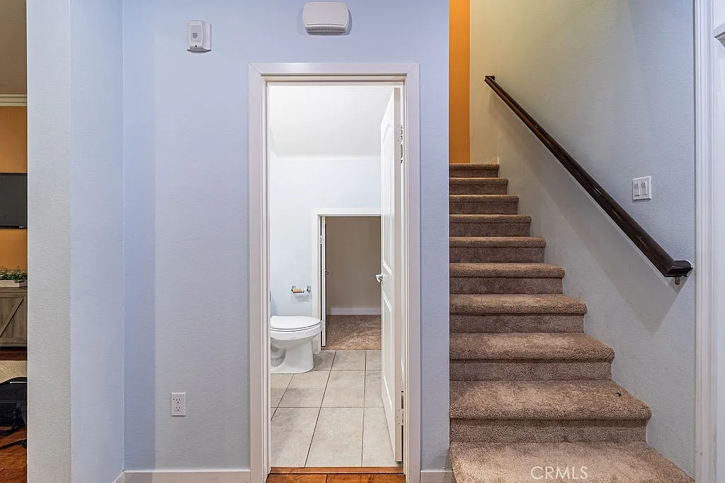 Hallway with light-colored walls, doorway to bathroom on left, and staircase with dark wooden railing.