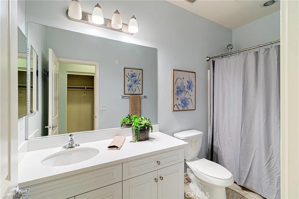 Bathroom with white vanity, sink, plant, large mirror, gray shower curtain, wall art, and neutral tile floor.